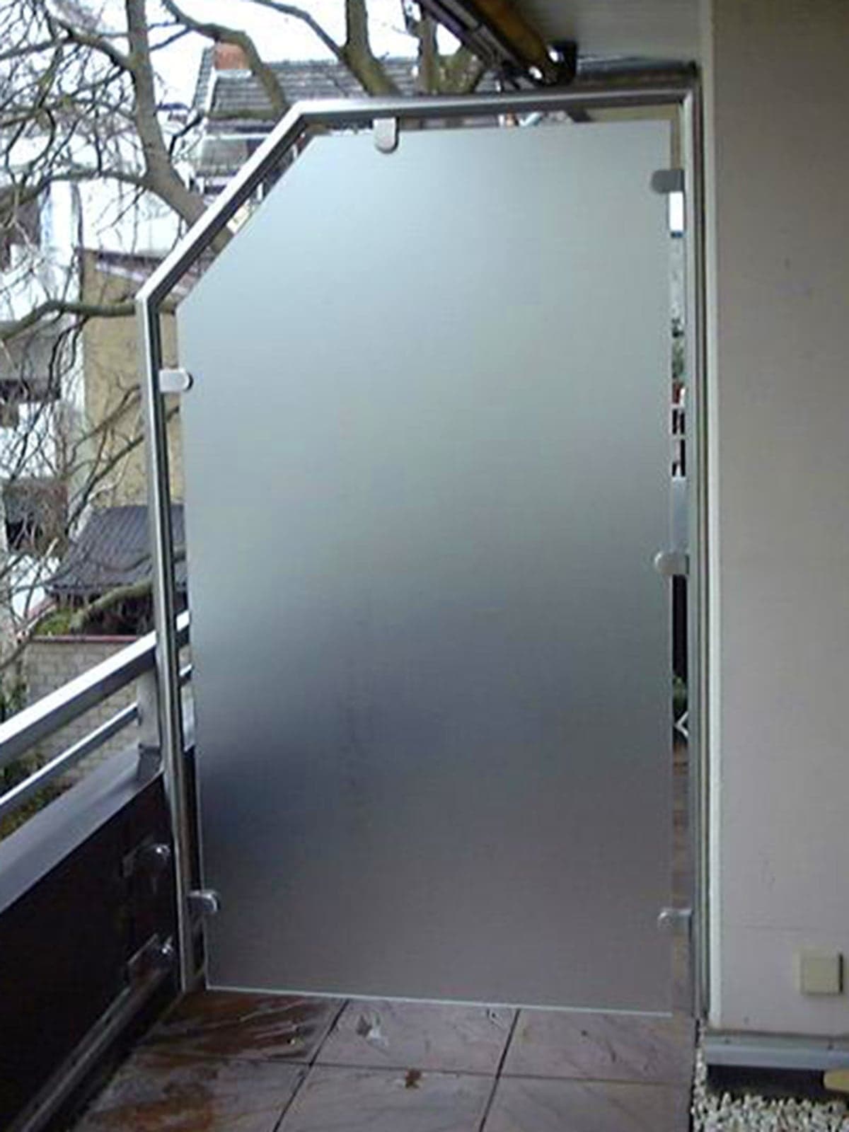 Satinierte Glastür mit Edelstahlrahmen auf einem Balkon als Sichtschutz und Zugangselement.