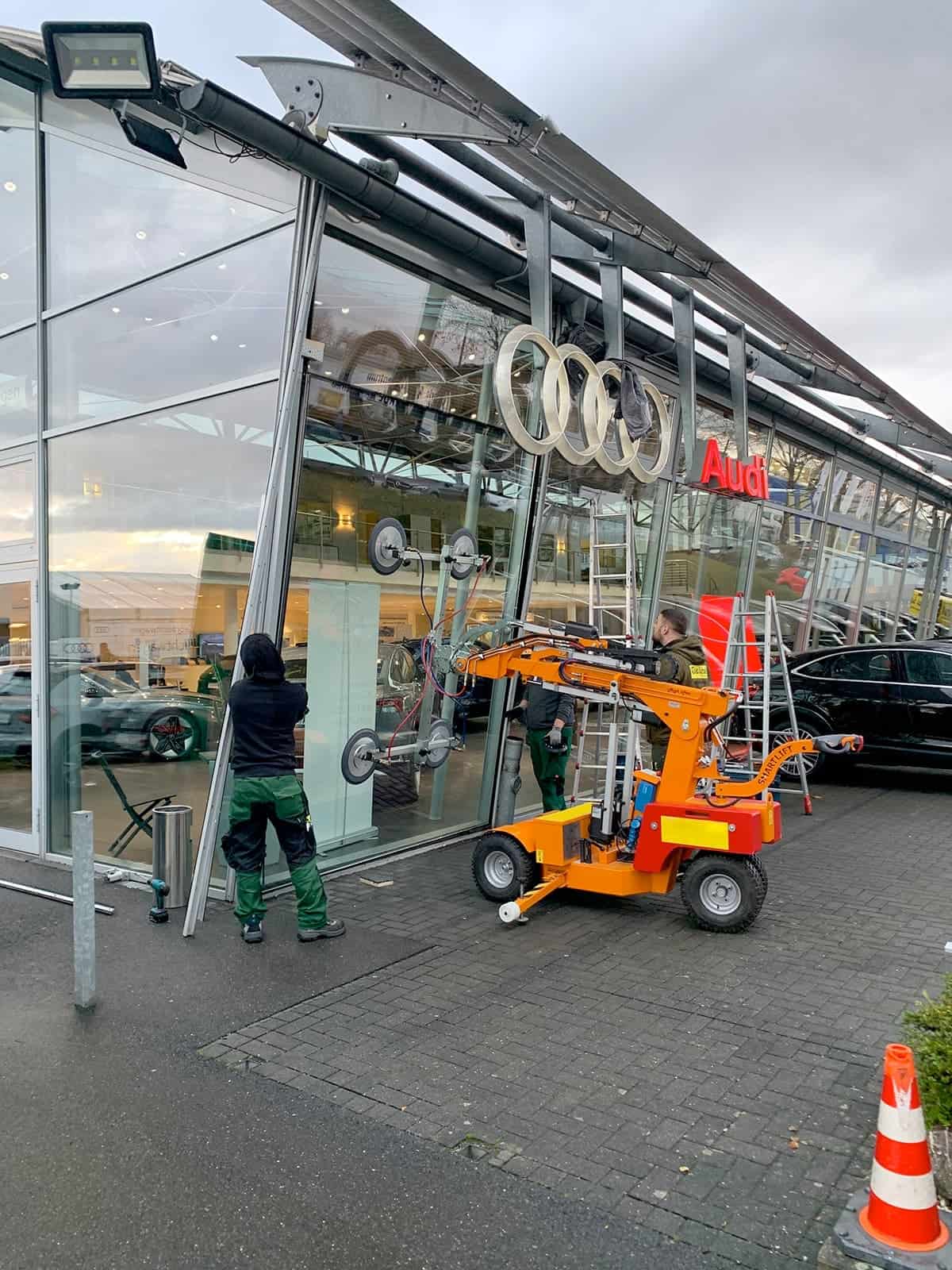 Glasarbeiter installieren mit einem Vakuumheber-Fahrzeug eine große Glasscheibe an einem Audi-Autohaus in Frechen.